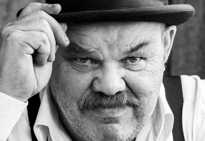 Kuvassa on Jaakko Teppo kasvokuvassa ja hän pitää oikealla kädellään mustan knallinsa reunasta kiinni. Kuva on musta-valkoinen.