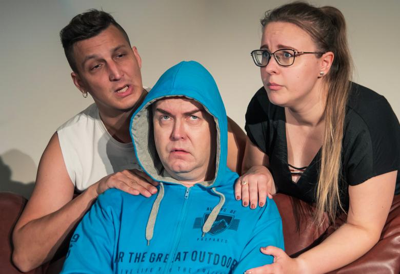 Kuvassa Antti Salmela istuu keskellä ruskealla sohvalla.  Sohvan takana ovat vasemmalla Arto Käki ja oikealla Marja Kuntsi kumartuneina Salmelan molemmilla puolilla.