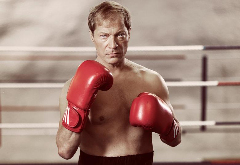 Kuvassa on Jukka.Pekka Mikkonen yläruumis paljaana ja punaiset nyrkkeilyhanskat kädessään ja mustissa housuissa. Taustalla näkyy valkoista nyrkkeilykehän aitaa.