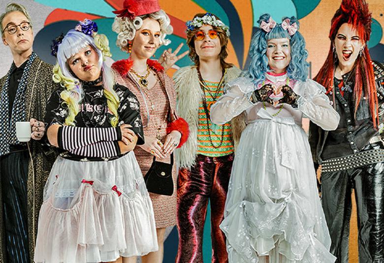 Kuvassa ovat nuoret näyttelijät ja heistä näkyvät kasvot, jotka ovat roolipukujen taulussa olevissa rei'issä. Vasemmalla on tumma miehen puku ja vieressä on tyttömäinen valkoinen runsas puolihame ja vaaleat kiharat. Keskellä on roosan värisessä mekossa nainen vieressään nuori mies tummassa, pitkässä tukassa ja kiiltävissä violeteissa housuissa. Oikealla on sinihiuksinen tyttö valkoisessa röyhelömekossa ja vieressään mustissa punk-vaatteissa oleva nuori nainen punaisine hiuksineen.