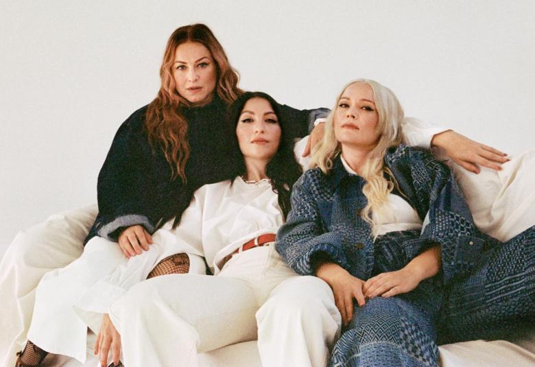 Kuvassa ovat sohvalla tiiviissä ryhmässä ja vasemmalla on Erin sinisessä puserossa ja valkoisissa housuissa istumassa. Keskellä on Ida Paul valkoisessa paidassa ja housuissa sekä oikealla Anna Puu sinisessä farkkupuvussa ja valkoisessa t-paidassa.  