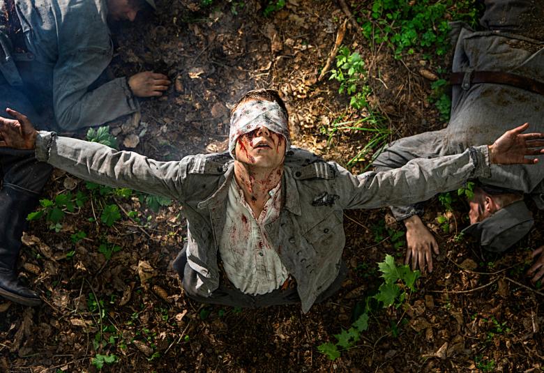 Kuvassa on sotilas maakuopassa side silmillään ja hänen takanaan on kaksi sotilasta kaatuneena maahan.