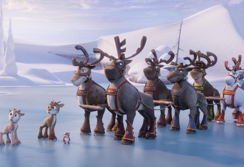 Kuvassa on jään päällä oikealla porolauma valjaissa. Edessä kaksi pientä poroa ja pieni orava. Taustalla on valkoinen tunturi.