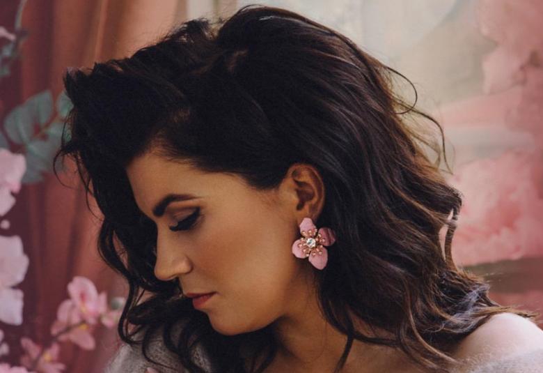 Kuvassa on Suvi Teräsniska sivuttain ja hänestä on puolivartalokuva. Hänellä on tummat pitkät, kiharaiset hiukset ja vaalea villapuseo. Taustalla on vaalean punaista verhoa ja vasemmalla vaaleanpunaisia  kukkia.