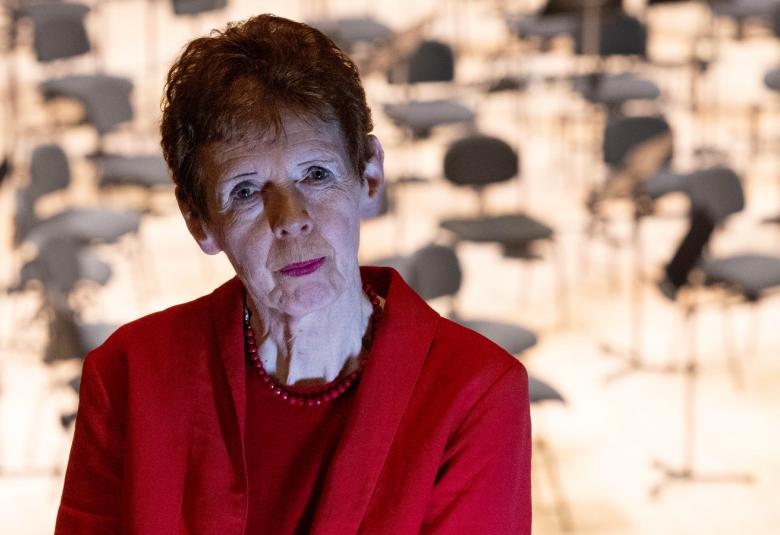 Kuvassa on Tuula Sarotie puolivartalokuvassa punaisessa jakussa. Taustalla näkyy orkesterin tyhjiä tuoleja. 