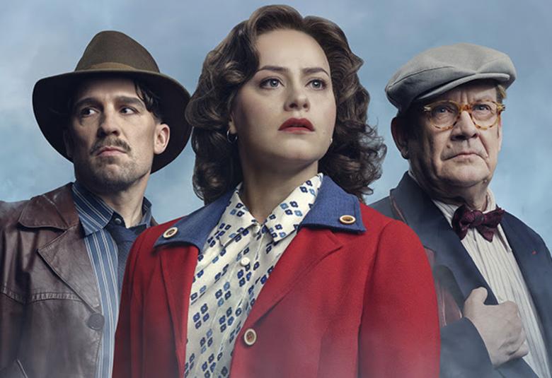 Kuvassa on puolivartalokuvassa vasemmalla mies, jolla tumma hattu ja musta nahkatakki. Hänen oikealla puolellaan on nainen, jolla on ruskeat pitkählöt lainehtivat hiukset ja tumman punainen takki. Oikealla on mies vaaleassa lippalakissa, tumman sinisessä takissa ja vaaleassa paidassa.