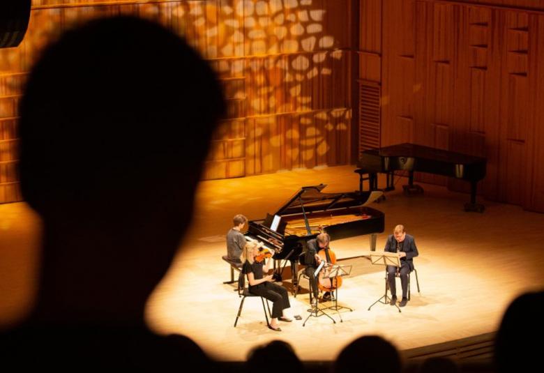 Kuvassa on neljään hengen kamariorkesteri soittamassa Kuhmo-salissa.  Kuva on kuvattu ylhäältä päin yleisön keskeltä ja ja yksi henkilö on vasemmalla isona.