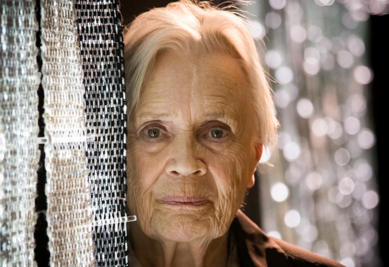 Kuvassa on Maija Lavonen kasvokuvassa.  Hänellä on vieressään hopeista kudottua tekstiilityötä ylhäältä alaspäin.  Taustalta näkyy hopeista kiiltoa.