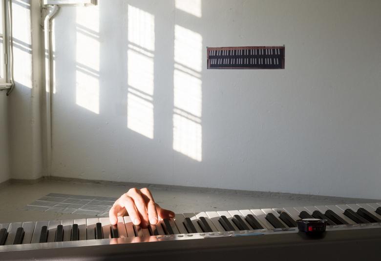 Kuvassa on alhaalla näkyvissä pianon koskettimet ja näkyvissä näkyy vain oikea käsi soittamassa. Taustalla näkyy huoneen kulma ja vasemmalla on ikkuna, josta tulee valoa ja se heijastuu neljänä osana seinälle.