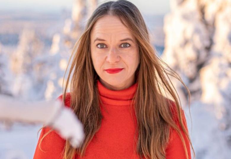 Kuvassa on Satu Rämö puolivartalokuvassa punaisessa puserossa. Hänellä on punertavat, pitkät hiukset. Taustalla on lumista ja lumen peittämää aavaa metsää.