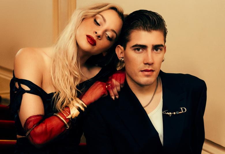 Kuvassa on Aliisa Syrjä vasemmalla ja hän nojaa robin Packalenin olkapäähän. Syrjällä on avokaulainen musta mekko päällään ja vaaleat pitkät hiukset. Packalenilla on musta takki. He molemmat istuvat ja kuva on puolivartalokuva. Tausta on kellertävä.