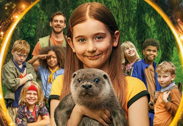 Kuvassa on keskellä kultaisen ympyrän keskellä Elma Ufacik, jolla on pitkät punertavat hiukset.  Hänellä on sylissää eteenpäin katsova saukko. Taustalla näkyy joukko lapsia ja yksi aikuinen mies.