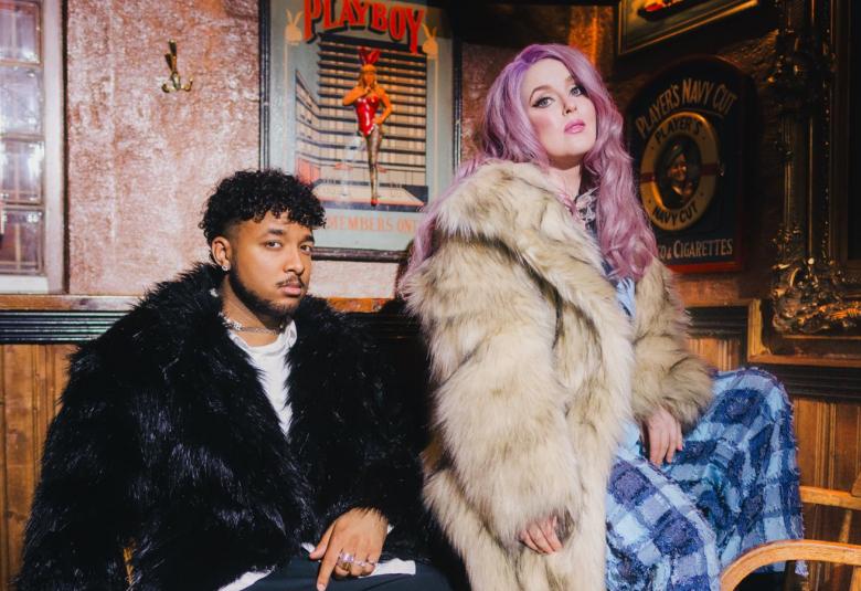 Kuvassa on vasemmalla istumassa Ani, jolla on musta pörröinen pusero. Vieressä vasemmalla on Ellinoora vaaleassa tekoturkissa. Hänellä on vaaleat violetit hiukset. Taustalla olevalla seinällä värikäs taulu oikealla ja keskellä harmaakehyksinen taulu, jossa on punainen naisfiguuri.