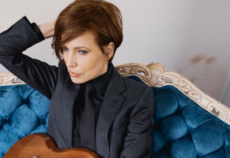 Kuvassa on Janita,joka istuu sinisellä topatulla sohvalla.  Hänellä on oikea käsi taivutettuna niskan taakse ja hän katsoo vasemmalle. Hänellä on tumman sininen jakku päällään ja hänellä on melko lyhyet punertavat hiukset.  Sylissään hänellä on ruskea kitara.