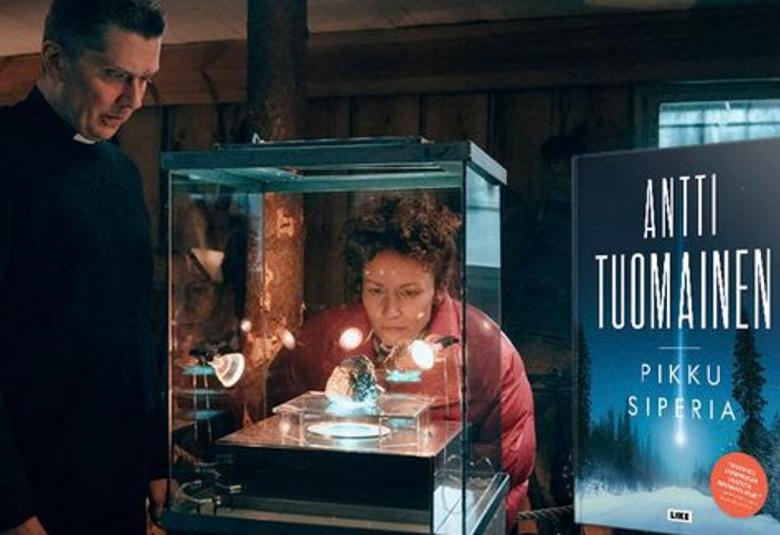 Kuvassa on vasemmalla Eero Ritala mustassa papin puvussa ja katsoo vitriiniä, jossa on hohtava kivi lasin päällä. Takana kumartuneena on nainen punaisessa toppatakissa katsomassa kiveä. Oikealla on kuva kirjan kannesta. Siinä on isoin kirjaimin Antti Tuomainen ja alla Pikku Siperia. Taustalla on kuva lumisesta maantiestä metsästä.  Taivas on tumman sininen ja siinä valkoinen meteoriitti. 