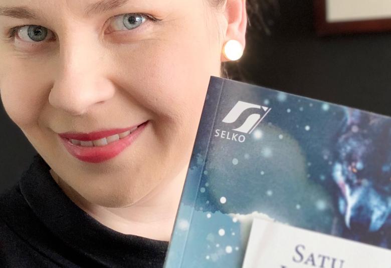 Kuvassa on Satu Leiskon kasvot ja alempana on vinosti osa kirjan kannesta, jossa on vaalean sinistä. Kuvan tausta on musta.