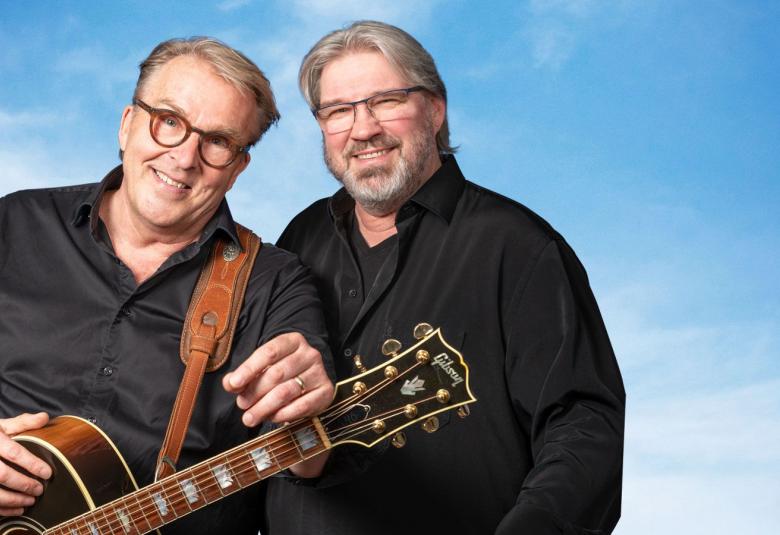 Kuvassa ovat Joel Hallikainen ja Pentti Hietanen vasemmassa reunassa puolivartalokuvassa mustissa puseroissa.  Hallikaisella on kitara kdessään.Tausta on sinitaivas.