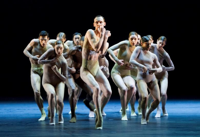 Kuvassa on joukko tanssijoita melko läpinäkyvissä harmahtavissa sukkapuvuissa. Tausta on tumma. Kaikki ovat melko kyyryssä menossa eteenpäin.