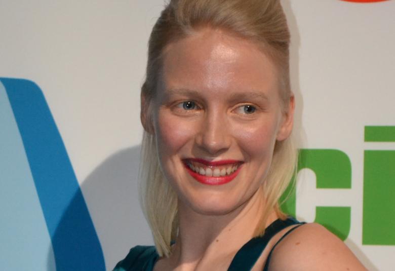 Kuvassa on Laura Birn kasvokuvassa ja hän poseeraa kuvaajille.  Taustalta näkyy oikealta vihreitä kirjaimia ja vasemmalta vihreitä kirjaimia.