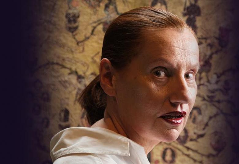 Kuvassa on puolivartalokuvassa Elina Mustonen ja hänellä on vaalea huppari päällään. Tausta on vasemmalta tummennettu ja pääosin ruskehtävän kuviollinen.