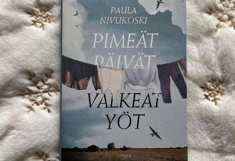 Kuvassa on keskellä kirja, jonka kannessa on ylhäällä pienemmin kirjaimin kirjoittajan Paula Nivukoski nimi ja isommin kirjaimin kirjan nimi Pimeät päivät ja mustin kirjaimin valkeat yöt. Taustalla on sini-valkoista taivasta, jssa lentää lintuja ja keskellä on pyykkinarulla pyykkejä. Alla on lakeaa peltoa. Taustana on valkista toppakanasta, jossa kultaisia hiutallekoristuksia.