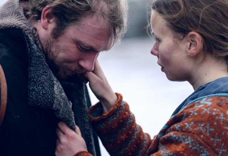 Kuvassa on puolivartalokuvassa vasemmalla paksussa tummas takissa ja hän katsoo alaspäin. Oikealla Amanda Jansson katsoo häntä ja auttaa käsillään takin kauluksen kanssa. Hänellä on letti hiuksissaan takana ja kirjava villapaita päällään.