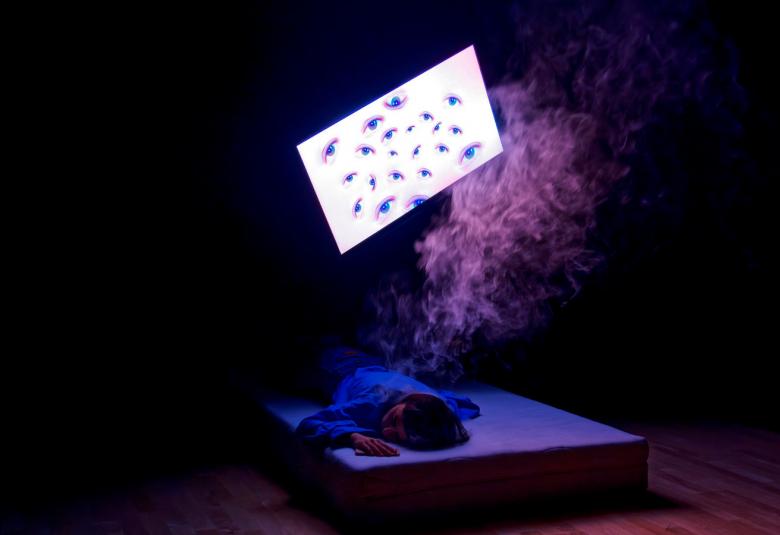  Kuvassa on tummalla taustalla on keskiosalla hieman valaistu alue ja siinä on lattialla sininen peti, jonka päällä makaa nainen. Takaa nousee höyryä ja vieressä on suorakaiteen muotoinen valkoinen alue.  Siinä on perhosen näköisiä kuvia.