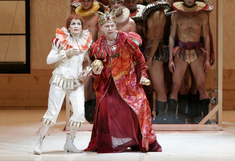 Kuvassa on valkoisessa harlekiinipuvussa. Vieressä on Jorma Uotinen oikealla pitkässä punaisessa pitkässä takissa. Taustalla on sotilaista puukehikon takana. 