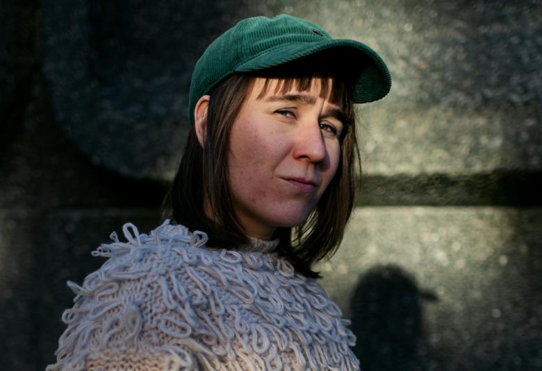 Kuvassa on Silja Viitala puoli hämärässä. Hänellä on sininen lippalakki päässään. Hänellä on vaalea pörhöllinen pusero. 