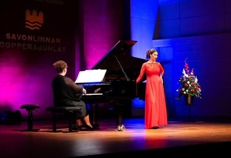 Kuvassa on vasemmalla vinosti selin Tuula Hällström soittamassa flyygeliä ja laulamassa Emma Kajander. Hän nojaa oikealla kädellään flyygeliin, jonka kansi on auki.  Kajanderin puku on punainen. Lava on tumma ja siinä on violettia ja sinistä valoa. Oikalla on kukkakimmpu jalustalla.