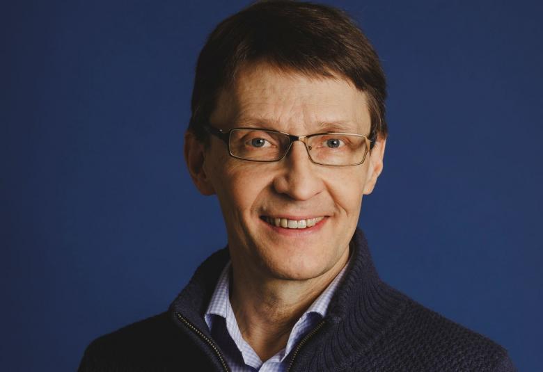 Kuvassa on Markus Nummi puolivartalokuvassa. Hänellä on tummansininen pusero ja vaalea paita. Tausta on tummansininen.