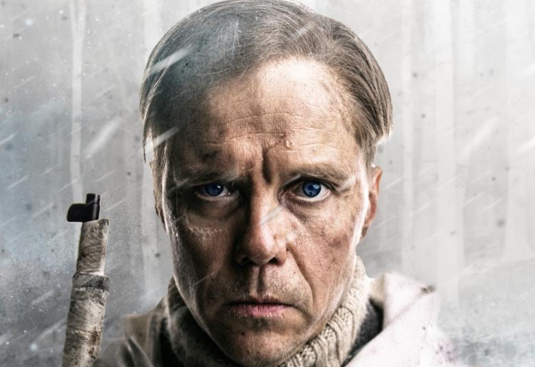 Kuvassa on Jarkko Lahti kasvokuvassa lyhyissä hiuksissa vakavailmeisenä. Kiväärin piippu näkyy vasemman olkapään yläpuolella. Taustalla on harmaata ja vinosti sataa lunta.