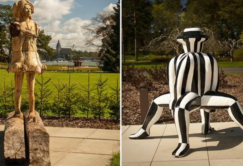 Kuvassa on kaksi kuvaa ja vasemmalla on kahden tukin päällä seisova haishahmo puusta, jolla on lyhypussihelmainen vaate päässä on huppu. Koko teos on vaalean ruskea. Taustalla on kesämaisemaa, jossa on nurmikko, järveä ja taustalla kirkon torni.  Oikealla on neljällä jalalla istuva hahmo, jossa on pullea yläosa.  Teos on musa-valkoraitainen.