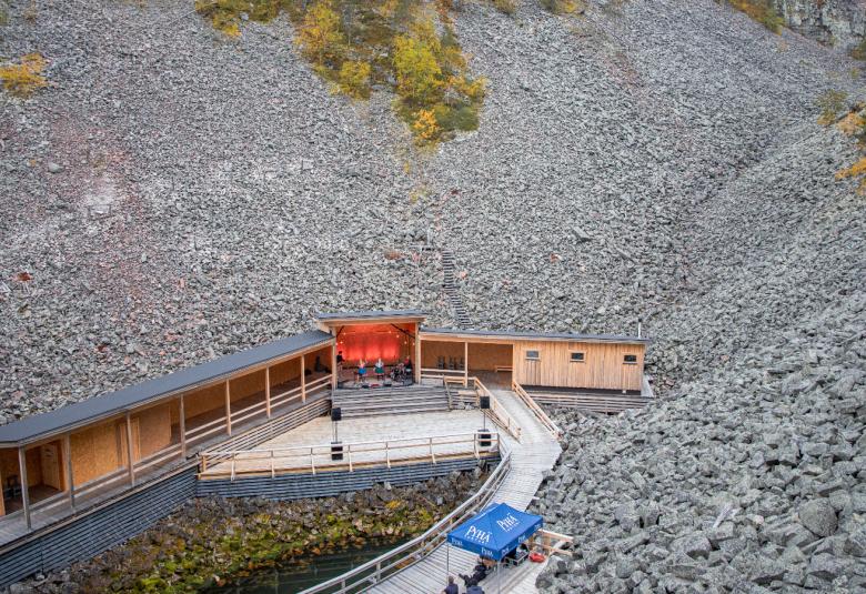 Kuvassa on kuru, jossa on molemmin puolin harmaata kiveä ja ulempänä vihreätä sammalta. Alhaalla on soikea esiintymislava.