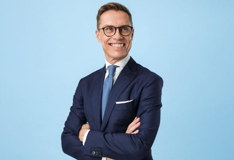 Kuvassa on Alexander Stubb puolivartalokuvassa. Hänellä on tumman sininen takki ja valkoinen paita sekä vaalean sininen kravatti päällään.  Tausta on vaalean sininen.
