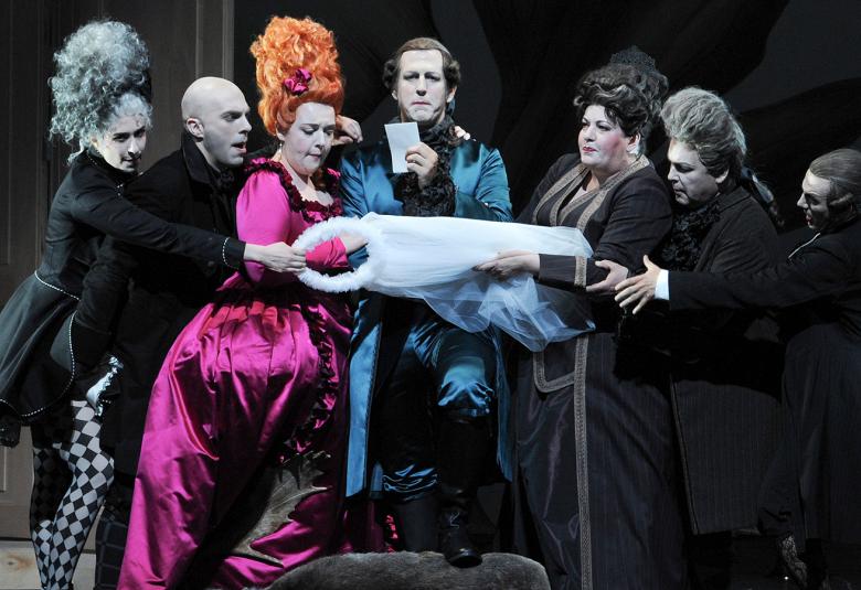 Kuvassa on hoviväkeä seitsemän henkilöä, joista reunimmaisella vasemmalla on korkea töyhtö päässään  ja kolmannella on pitkä violetti päällään. Kaikki pitelevät valkoista huntua käsissään.