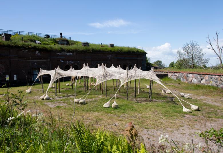 Kuvassa on valkoinen harsokattoinen aurinkosuoja ruohoisella maalla ja vallien ympäröimänä. taustalla on sinistä taivasta.