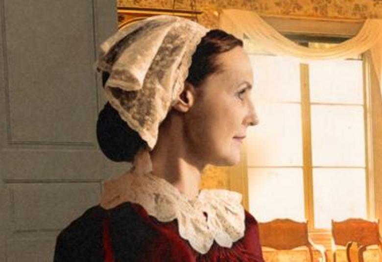 Kuvassa on puolivartalokuva naisesta, joka on sivuttain ja jolla on pitsinen hilkka ja kaulus sekä burgundin punainen mekko. Kuva on osa kirjan kannesta.