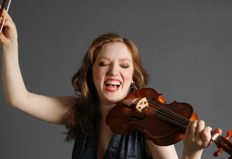 Kuvassa on Rachel Barton Pine oikea käsi ojennettuna ylöspäin toisessa kädessään viulu. Hänellä on kiharat, pitkät punertavat hiukset. Tausta on harmaa.