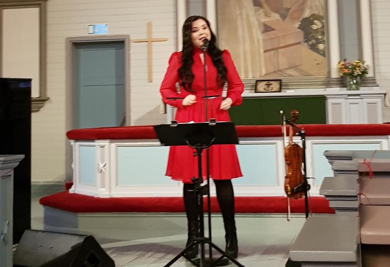 Kuvassa on Diandra laulamassa Virolahden kirkon alttarin edessä punaisessa mekossa.