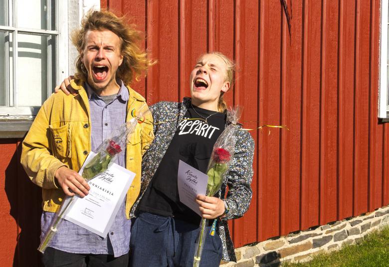 Kuvassa ovat Erkki Virkkala keltaisessa takissa. Oikealla hänen vieressään on Iikka Huntus harmaassa takissa ja mustassa t-paidassa. Molemmat ovat innoissaan. Takana on punaista talon seinää ja valoinen ikkuna. 