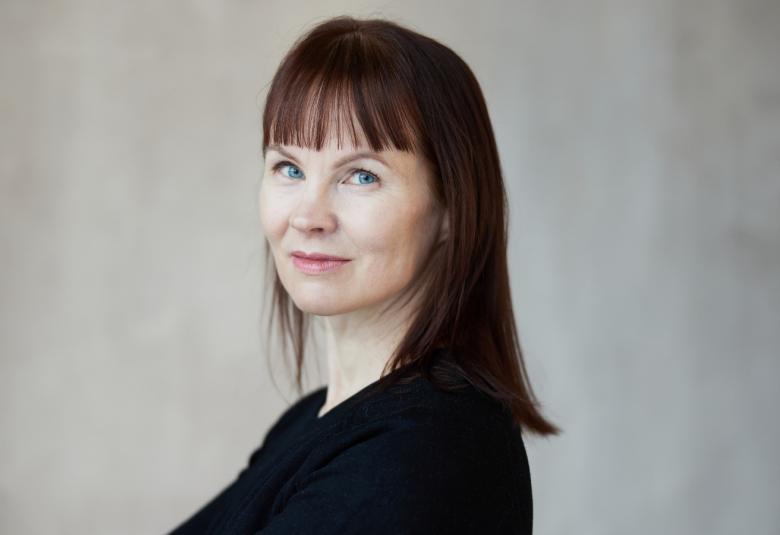 Kuvassa on Marisha Rasi-Koskinen puolivartalokuvassa ja hänellä on musta t-paita ja pitkät suorat hiukset. Tausta on harmaa.