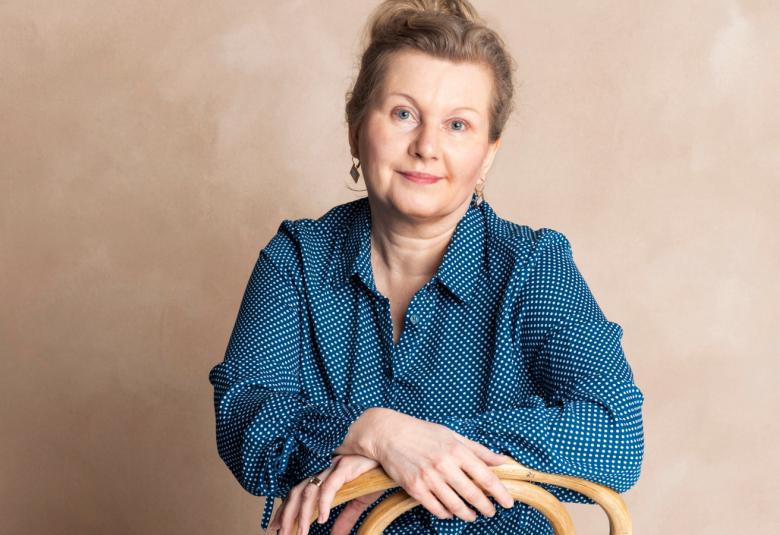 Kuvassa Tuula Salminen istumassa ja hänellä on käsivarret ristikkäin edessään. Hänellä on sininen pusero päällään. Tausta on ruskehtava.