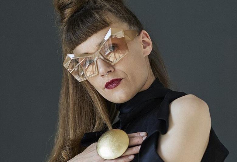 Kuvassa on Josefine Opsahl puolivartalokuvassa ja hänellä on suuret monikulmaiset, läpinäkyvät silmälasit ja tummahko tukka ylänutturalla sekä hiuksia hajallaan. Kädessään hänellä on iso, pyöreä sormus. Tausta on harmaa.