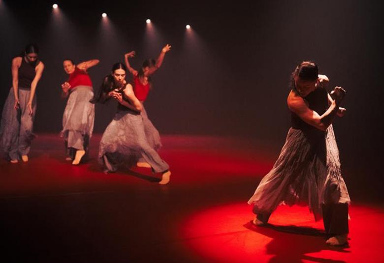 Kuvassa on vasemmalla punaisessa alokeilassa neljä tanssijaa ja oikealla yksi tanssija. Tausta on tumma.