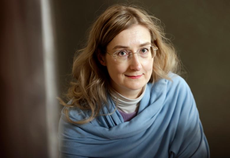 Kuvassa on Emmi Itäranta puolivartalokuvassa. HÄnellä on pitkähköt ruskeat hiukset olkapäille.  Hänellä on vaalean sininen pusero päällään. Taustalla on ruskeaa verhoa.