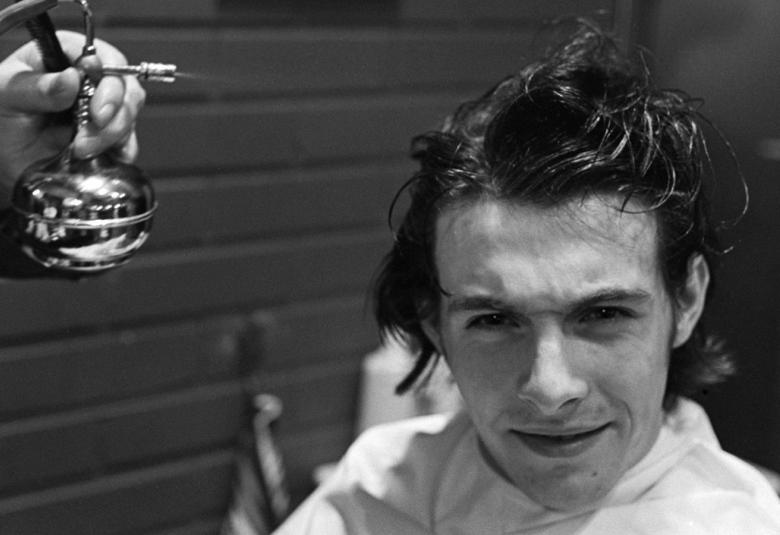 Kuvassa on vasemmalla käsi, jossa on kilautettava kello. Oikealla alhaalla on Kirkan kasvokuva.  Kuva on musta-valkoinen.