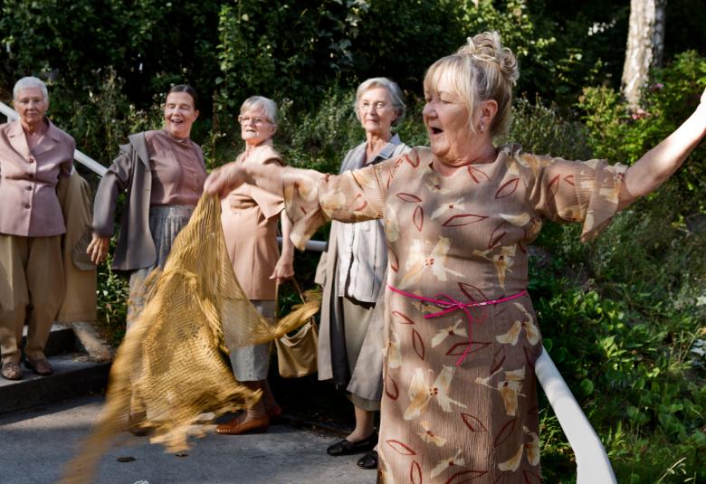 Kuvassa on viisi naista juhlavissaä puvuissa ulkona metsäisessä paikassa.He ovat jonossa.