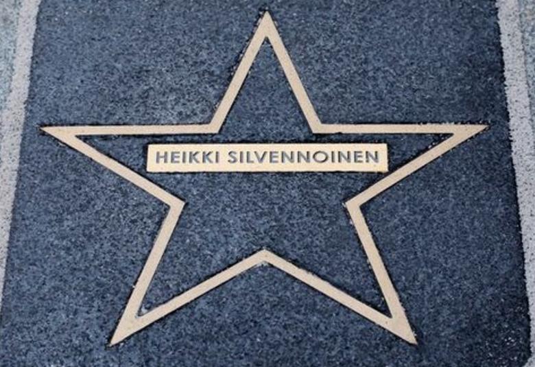Kuvassa on keskellä kullan värinen iso tähti kadussa tummalla asfaltissa ja siinä on nimikilpi, jossa lukee Heikki Silvennoinen.  Reunoilla on vaaleampaa asfalttia. 