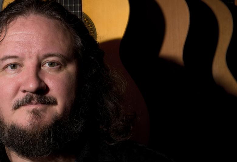 Kuvassa on Tomi Tolvasen kasvokuva vasemmalla ja hänellä on tummat, pitkät hiukset ja leukapartaa sekä viikset. Taustalla on keltainen ja ruskeaita sekä mustia, paksuja raitoja ja alaosa on tumma. 